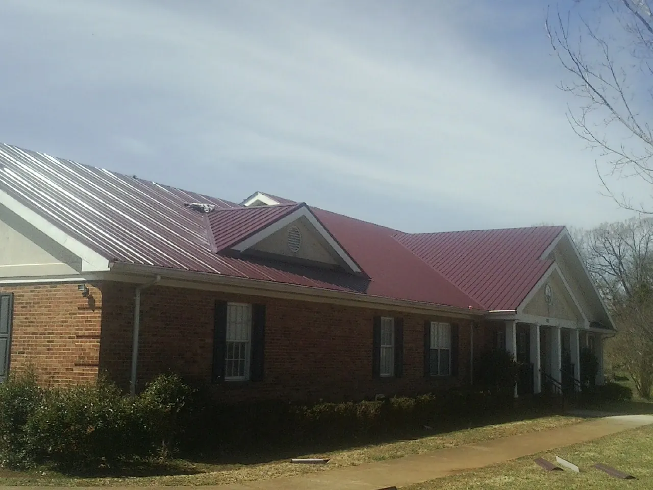 Red metal roof with gabled entries on a long brick building, from a Hail Damage Roof Repair job in Hyannis