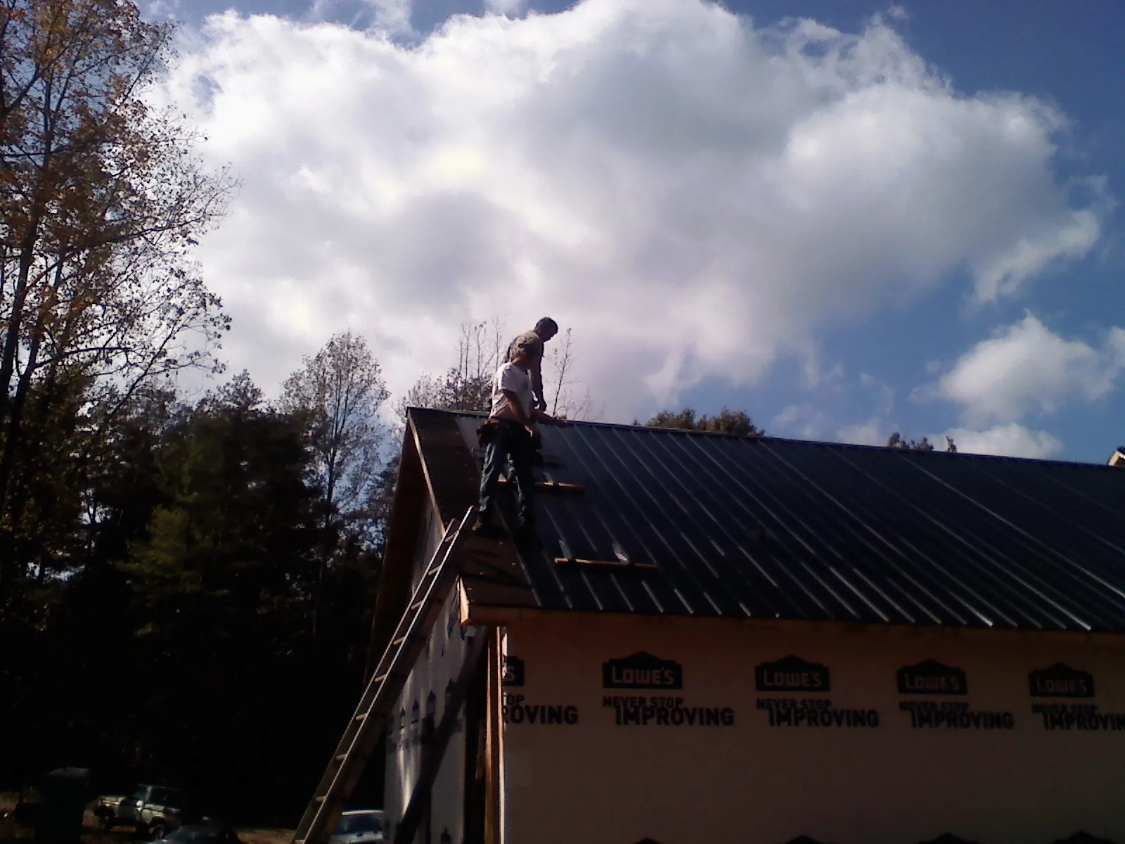 Roofer fastening dark metal panels high against a cloudy sky, from a Roof Inspection job in Hyannis