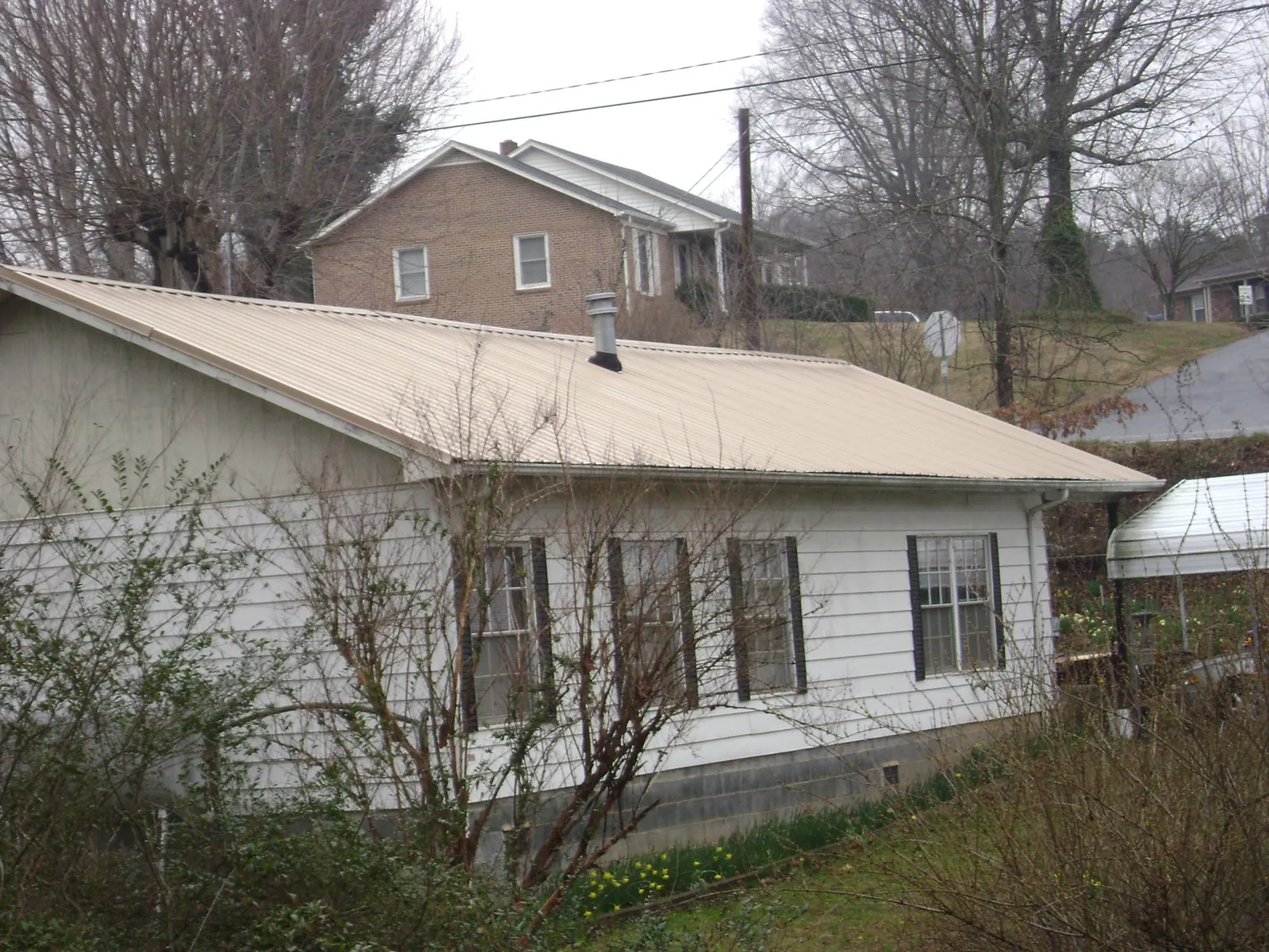 Tan metal roof on a white sided house set into a hillside — Commercial Roofing by Roofing Brothers in Hyannis