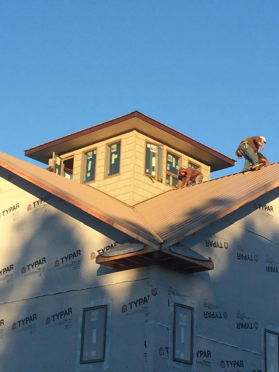 Roofers working around a rooftop cupola on a new metal roof at sunset — Roof Waterproofing in Hyannis by Roofing Brothers